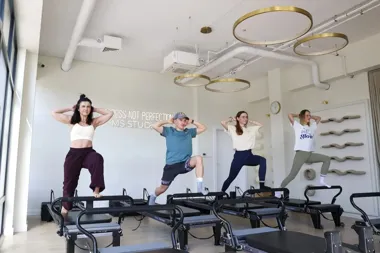 Cztery osoby ćwiczą pilates na reformerach w jasnym studio.