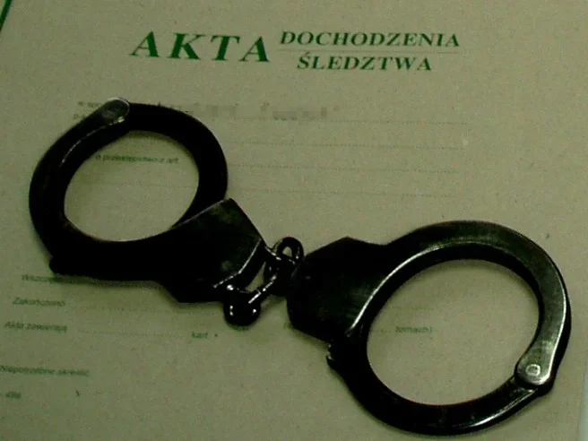 Metalowe kajdanki leżą na dokumentach akt dochodzenia śledztwa.