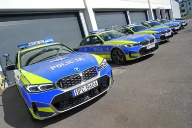 Szereg oznakowanych radiowozów marki BMW zaparkowanych przed garażami.