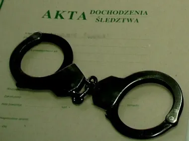 Metalowe kajdanki leżą na dokumentach akt dochodzenia śledztwa.